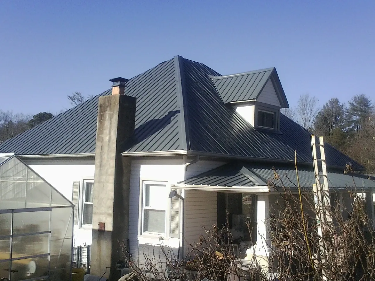 Dark blue standing seam metal roof on a white farmhouse with dormer — Slate & Tile Roof Repair by Roofing Brothers in Brookfield