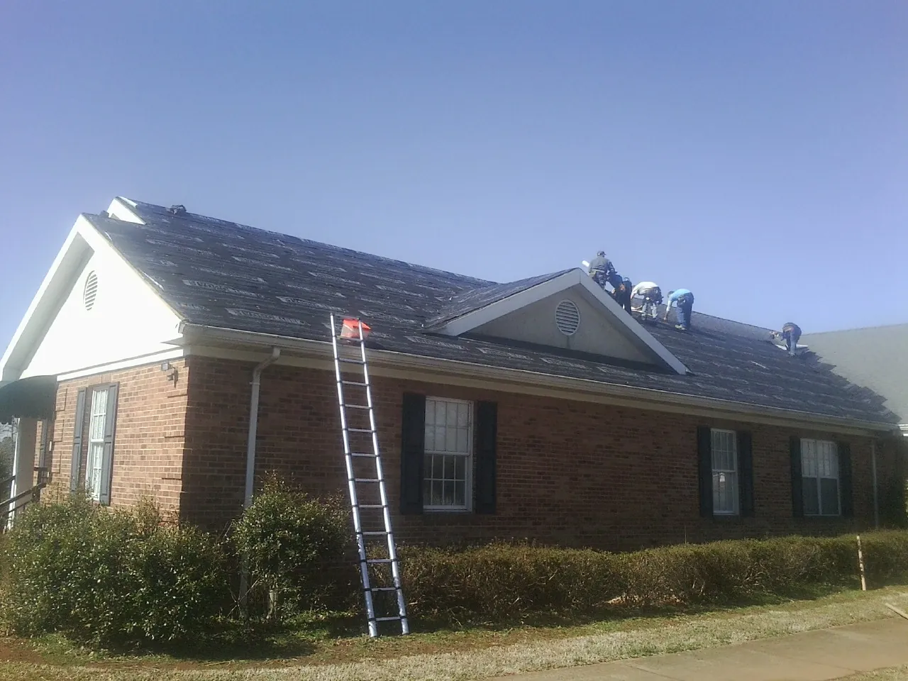 Crew tearing shingles off a brick ranch roof with a ladder set — Emergency Roof Repair work by our crew in Brookfield